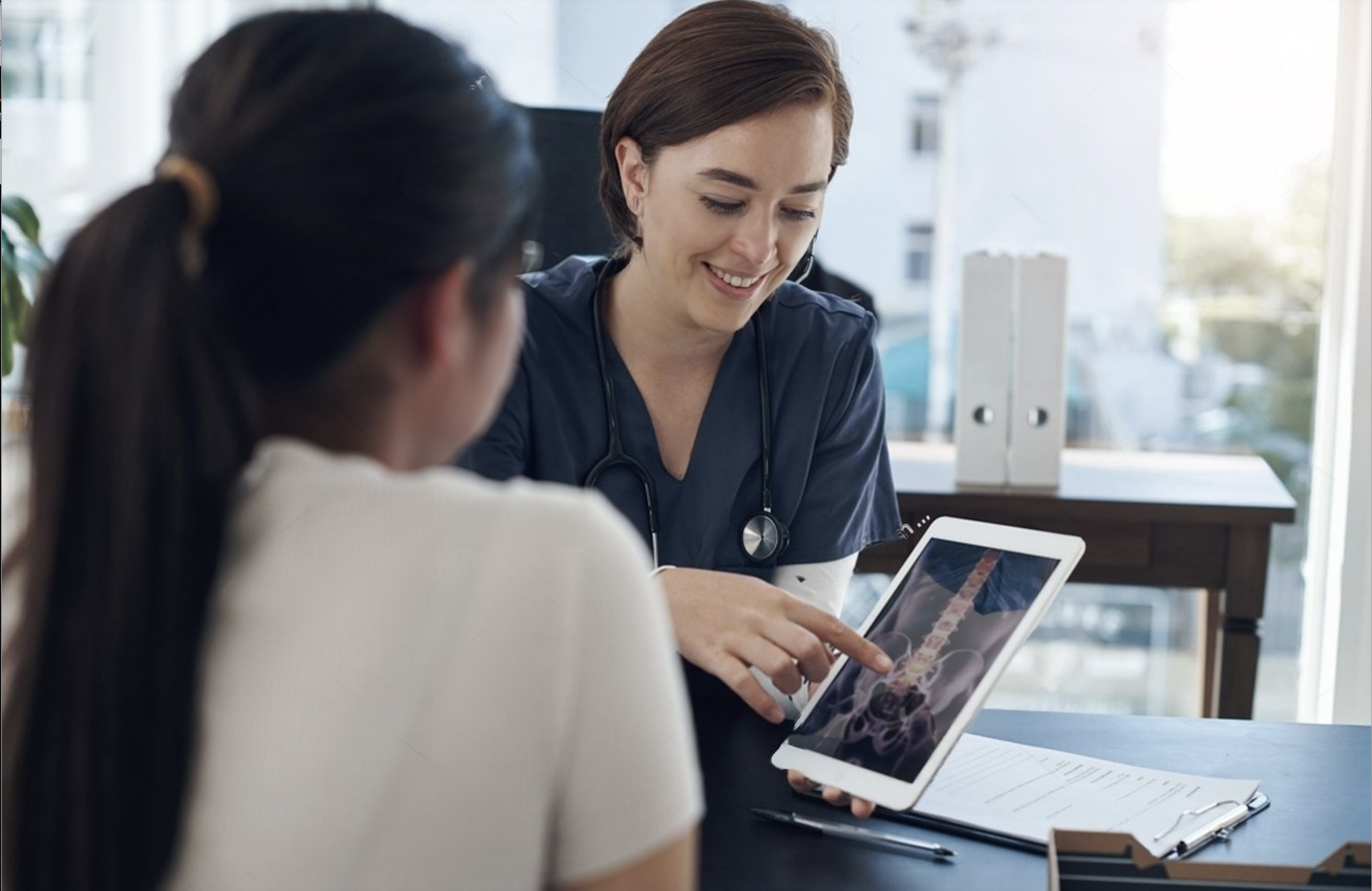 Paciente accediendo a sus imágenes médicas (columna vertebral) en una tablet junto a su doctora